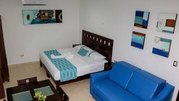 Habitació d'hotel amb un llit, un sofà blau, una taula de dinar i obra d'art a les parets.
