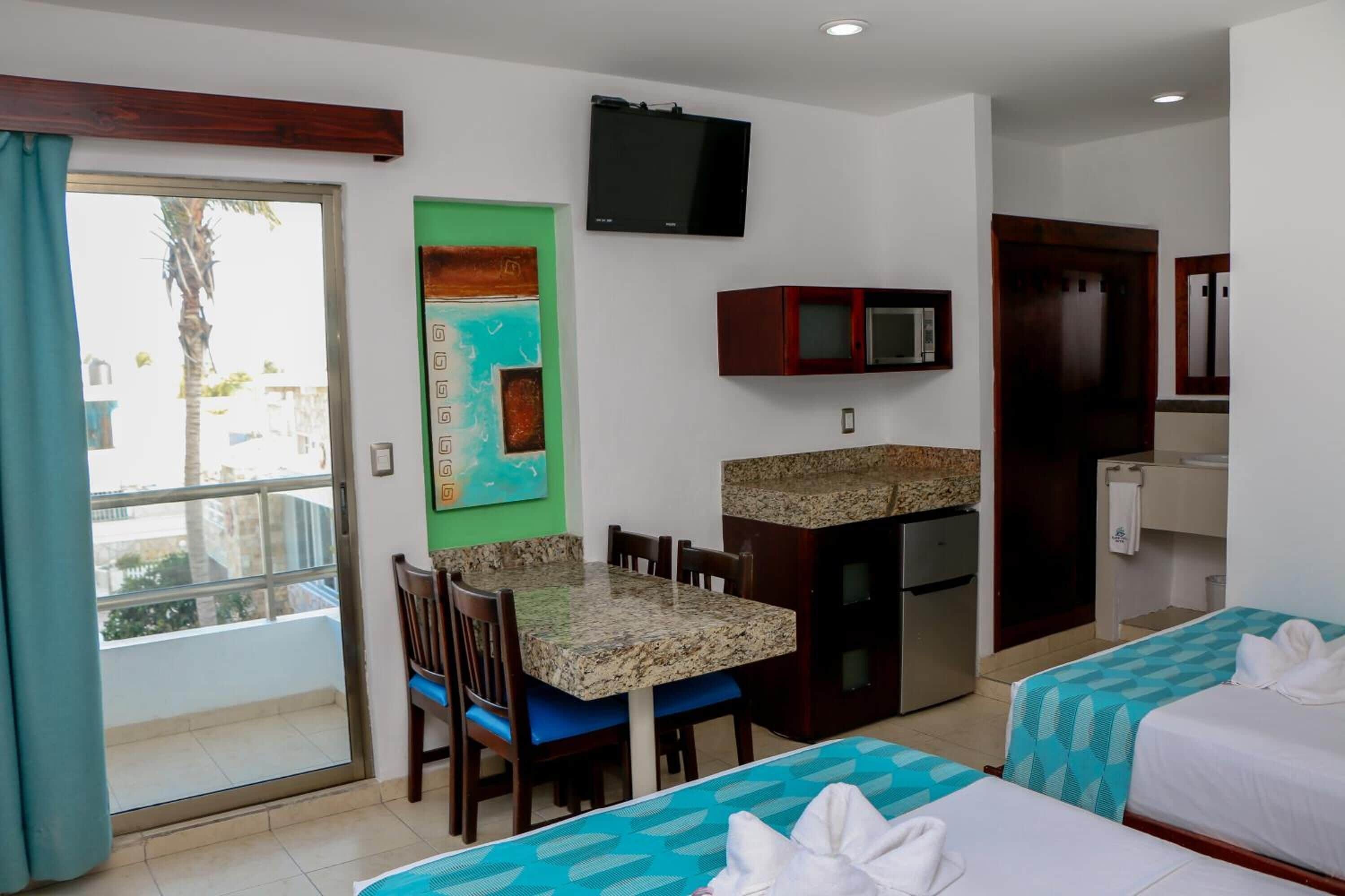 A hotel room with a dining area, kitchenette, and two beds.