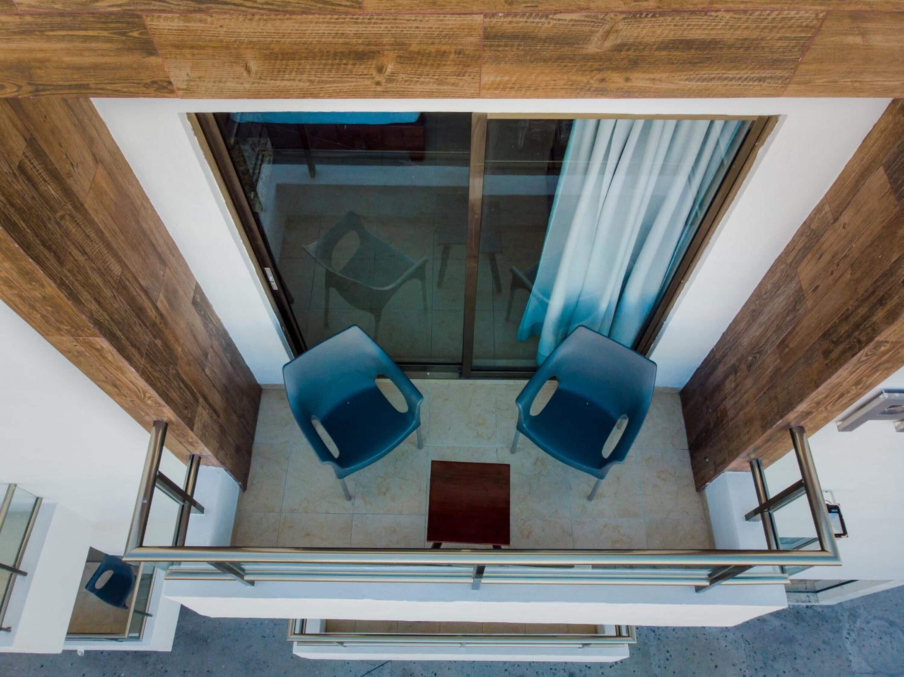 A balcony with two blue chairs, a small table, and a glass door leading to an interior space.