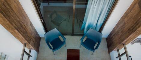 A balcony with two blue chairs, a small table, and a glass door leading to an interior space.