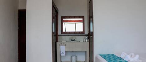 Habitación de hotel con cama, baño con lavamanos y espejo, y una puerta que da a otra habitación.