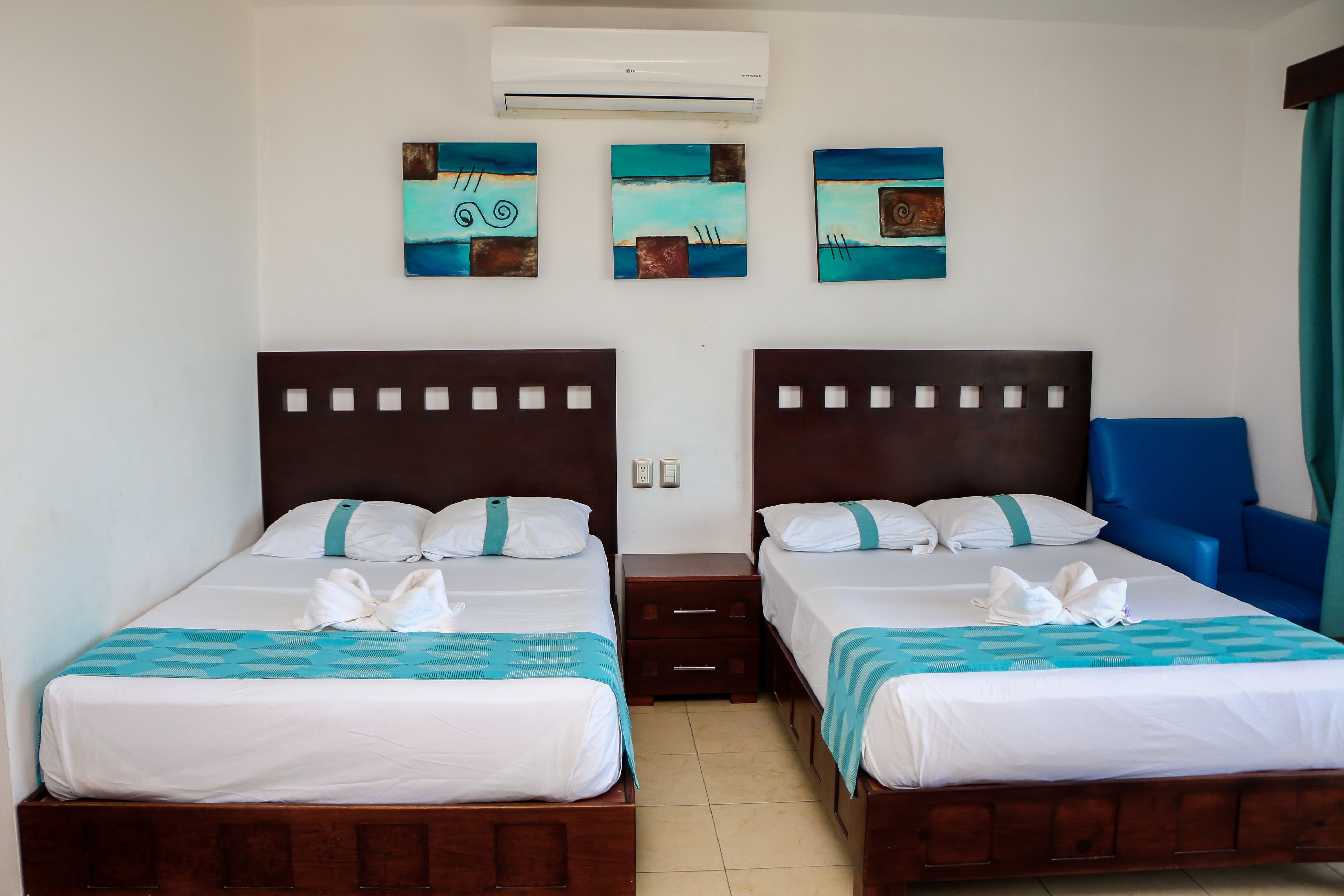 A hotel room with two beds, a blue chair, and artwork on the wall.