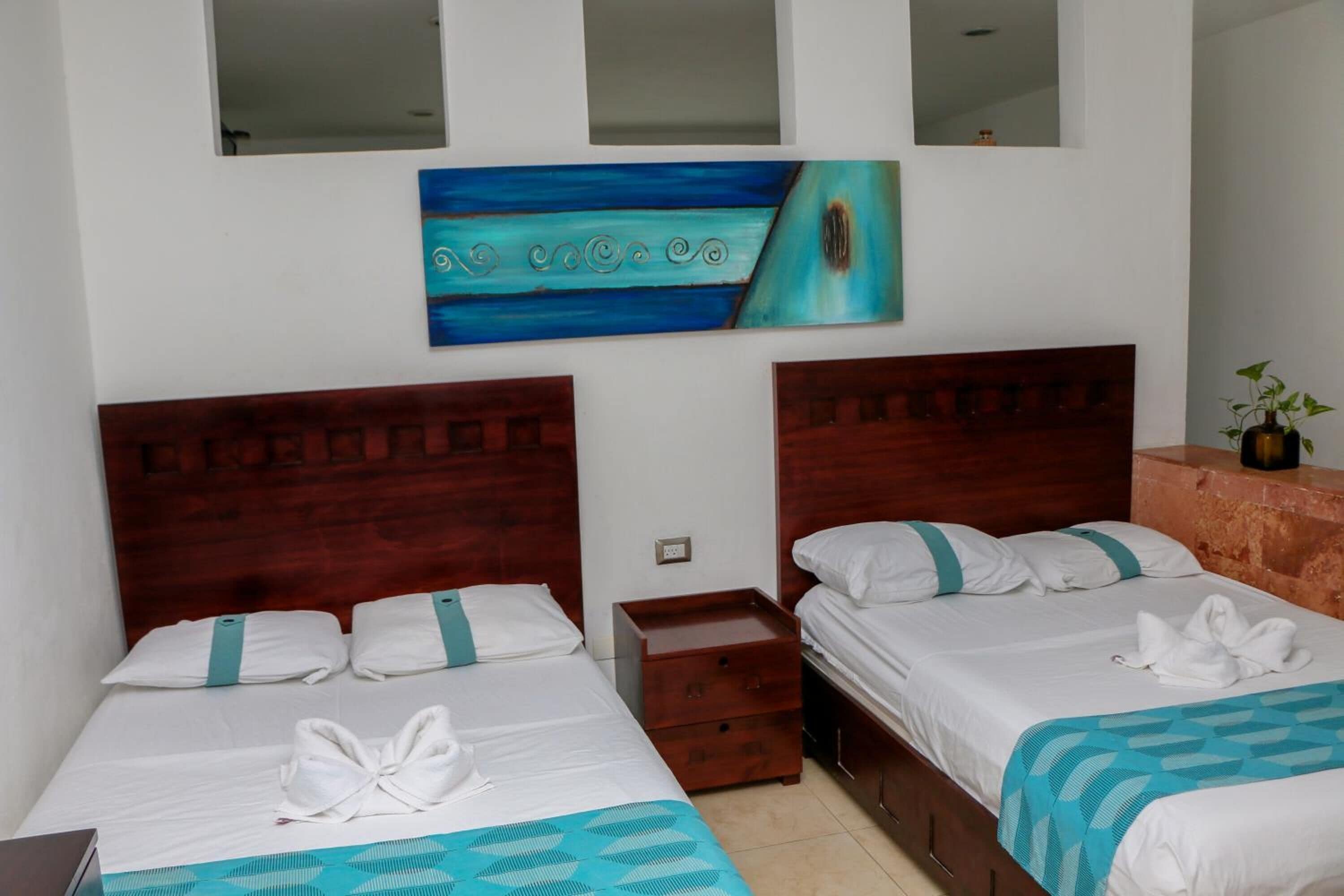 A hotel room with two beds, a wooden headboard, a small wooden nightstand, and a painting on the wall.