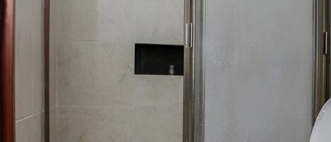 A bathroom with a glass-enclosed shower, a toilet, and a small mirror above the sink.