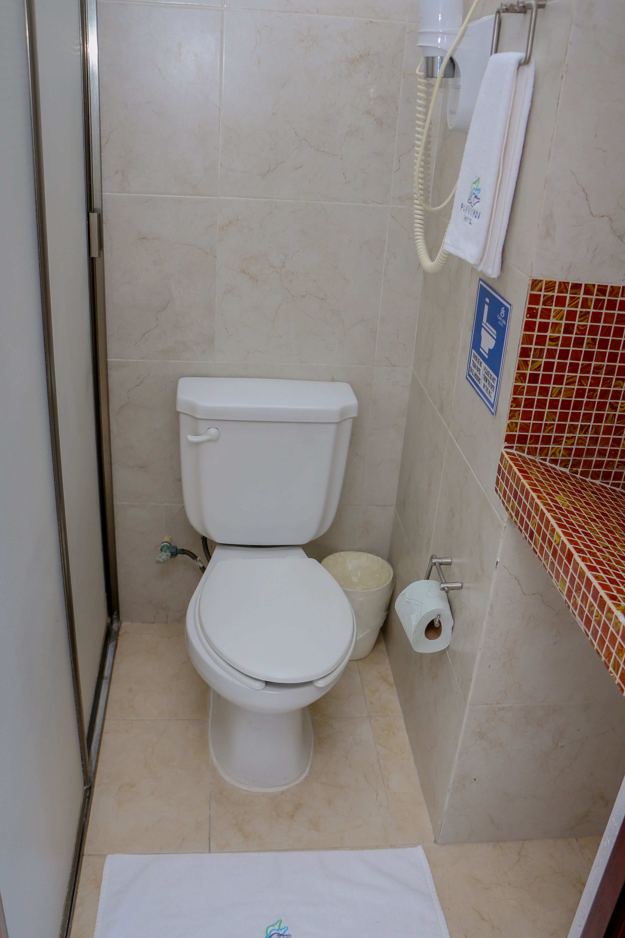Ein Badezimmer mit Toilette, einem Händetrockner, einem Handtuchhalter und einer Toilettenpapierrolle.