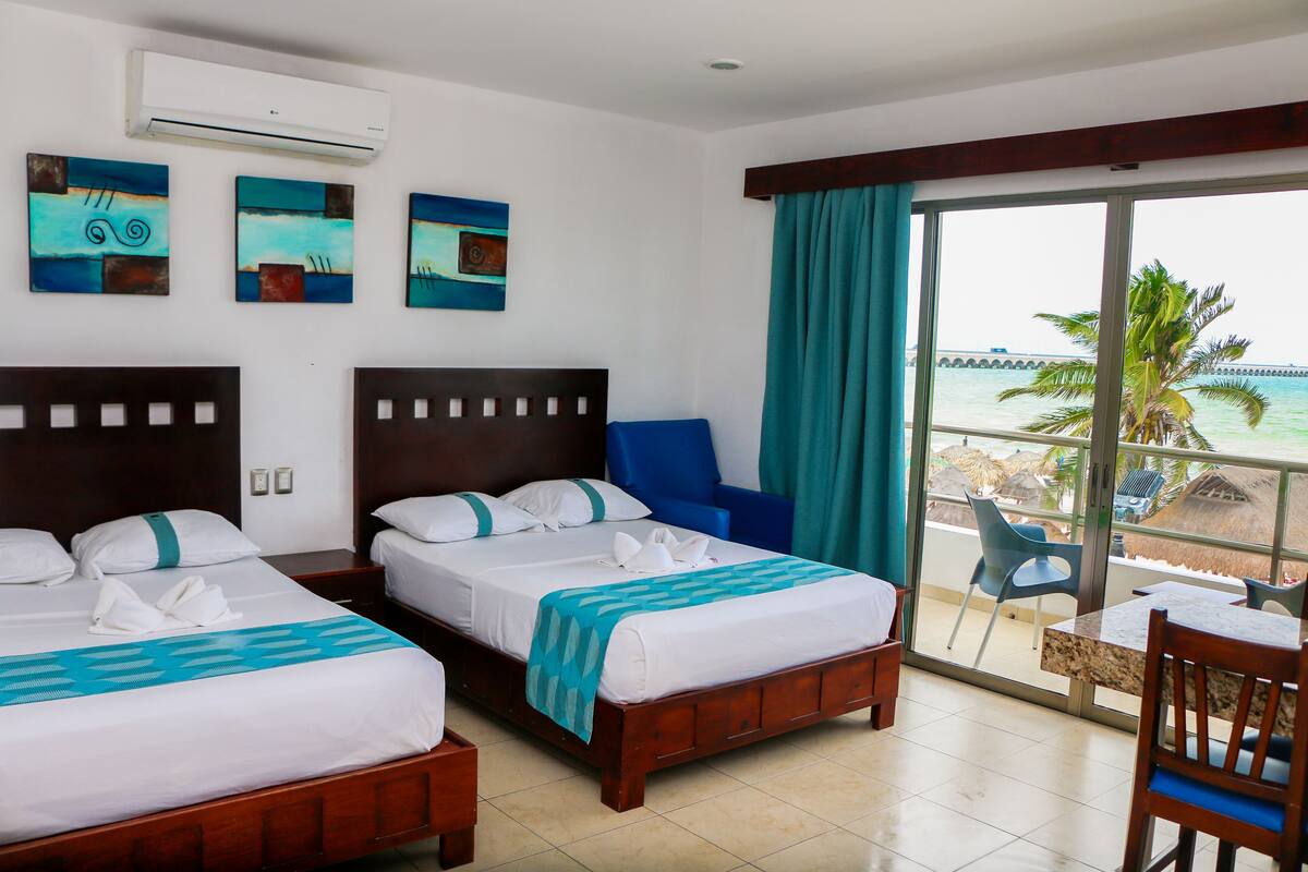Quarto de hotel com duas camas, varanda e vista para o mar, e obras de arte na parede.