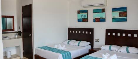 A hotel room with two beds, a bathroom, and artwork on the walls.