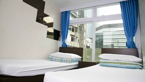 Habitación de hotel con dos camas, un ventanal con cortinas azules y vistas a edificios.