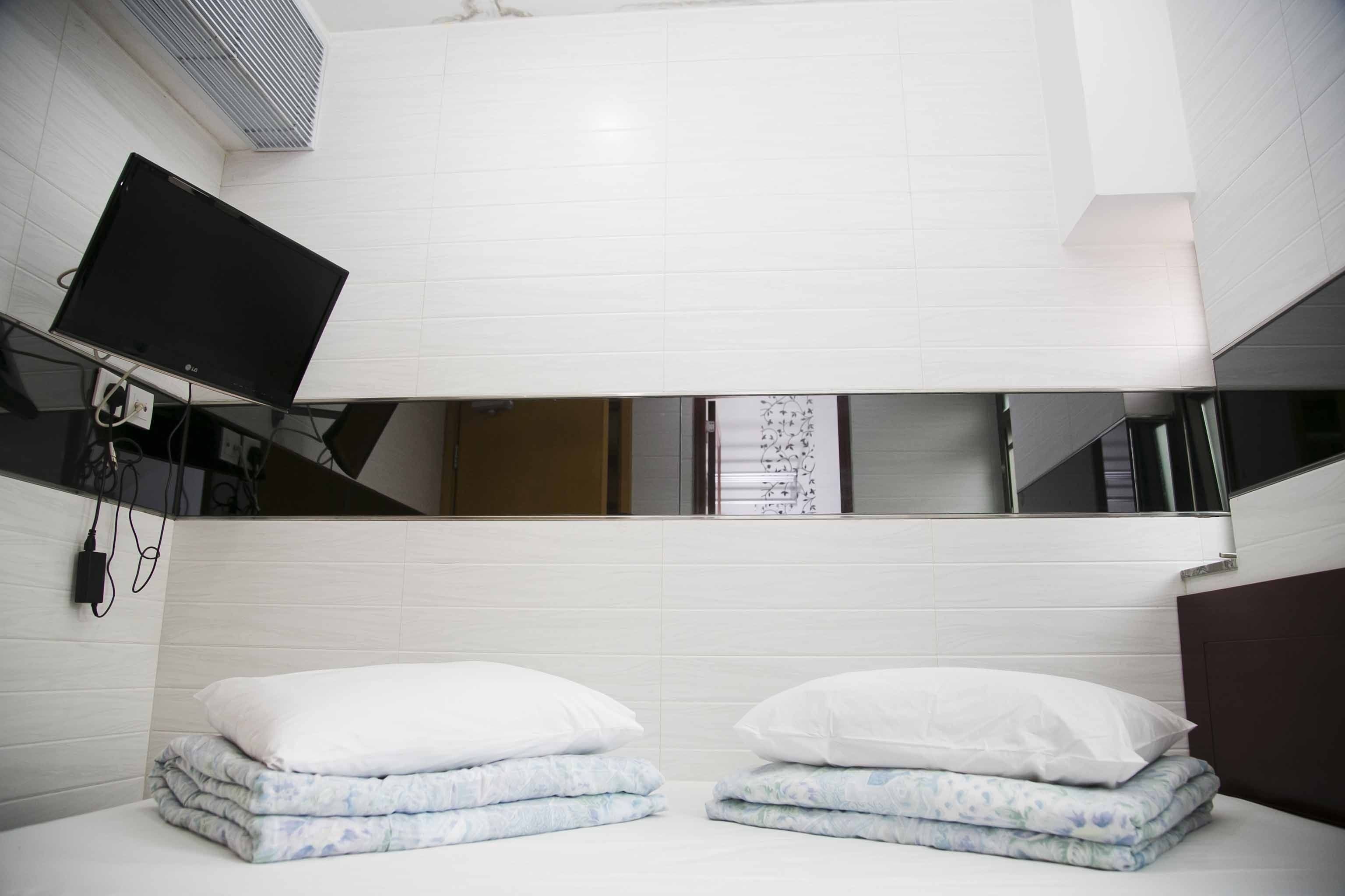 A hotel room with a bed, a TV mounted on the wall, and a mirror above the bed.