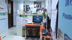 Zona de recepción con escritorio, computadora y asientos. Hay tablones de anuncios con avisos y un calendario.