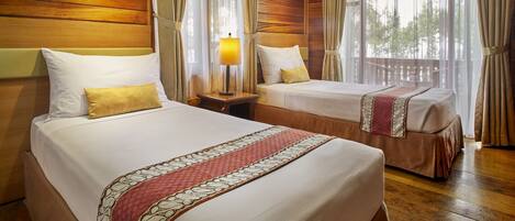 A hotel room with two beds, wooden paneling on the walls, and large windows with curtains.