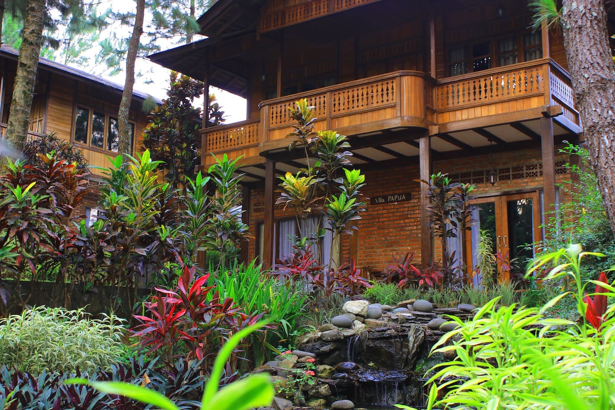 A wooden building with a balcony, surrounded by lush tropical plants and a small waterfall.
