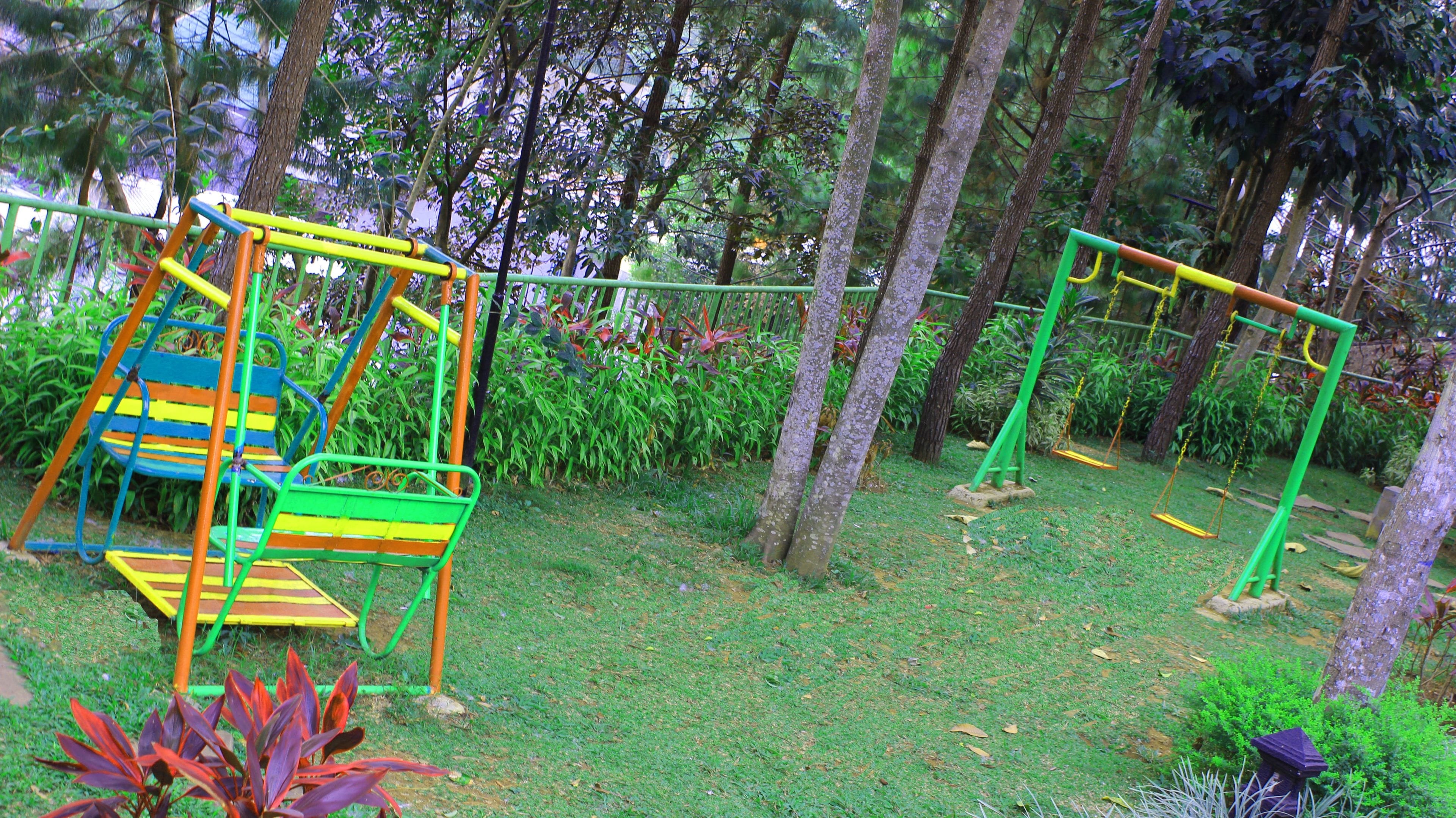 Un parque infantil con columpios y un tobogán, rodeado de árboles y césped.