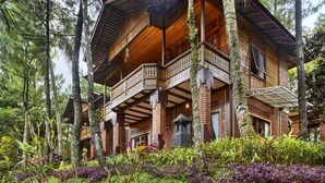 Eine große, mehrstöckige Holzhütte mit Balkon, umgeben von dichtem Wald.