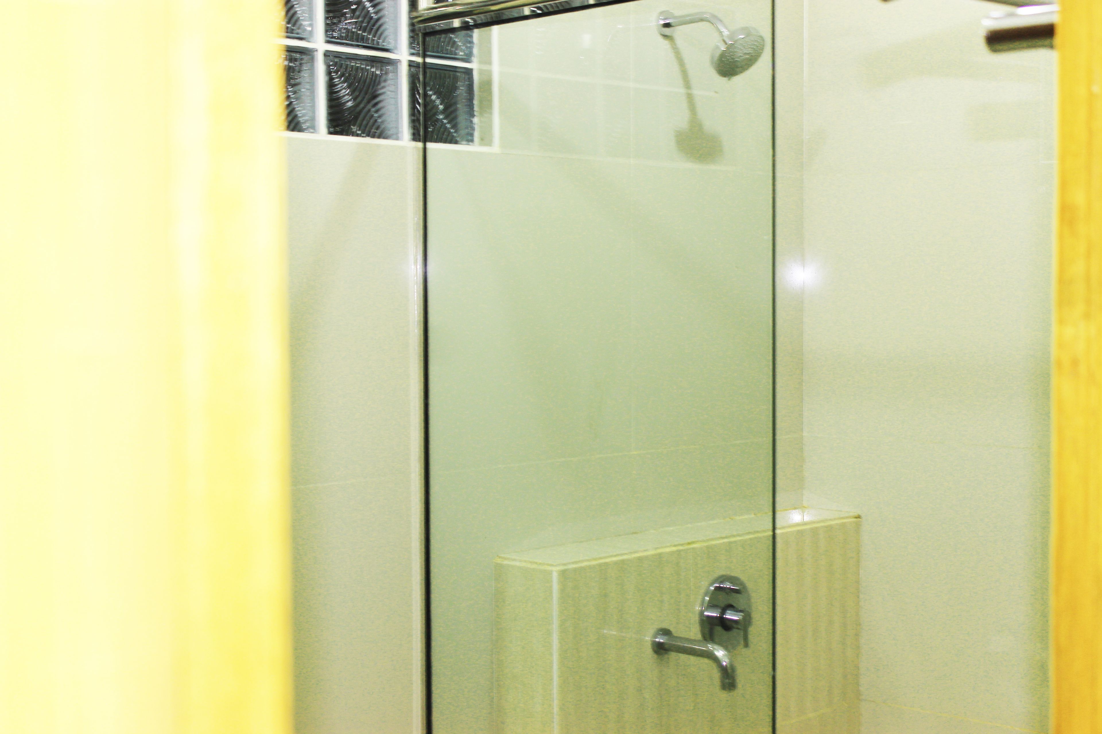 A glass-enclosed shower with a handheld showerhead and a control panel.
