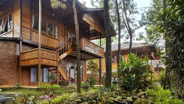 Eine Holzhütte mit Balkon, umgeben von dichtem Grün und Bäumen.