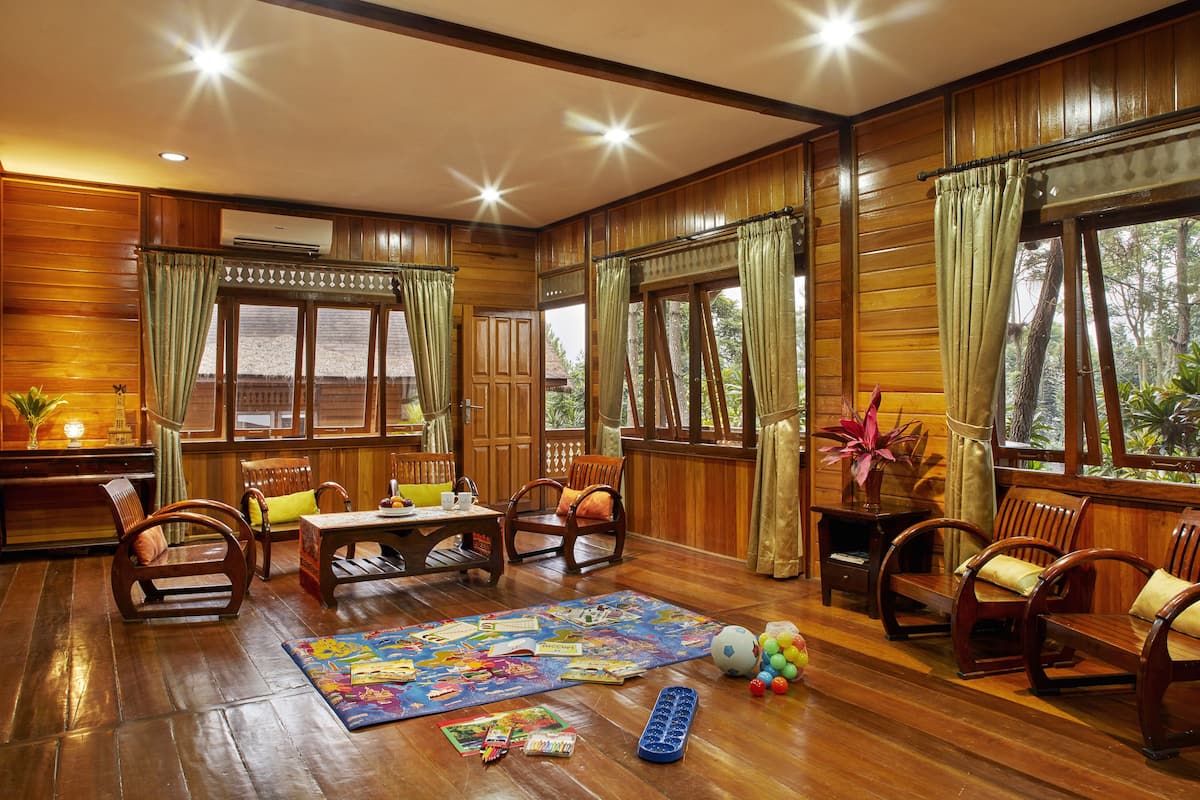A wooden-floored room with a large window, a puzzle on the floor, and several wooden chairs and tables.