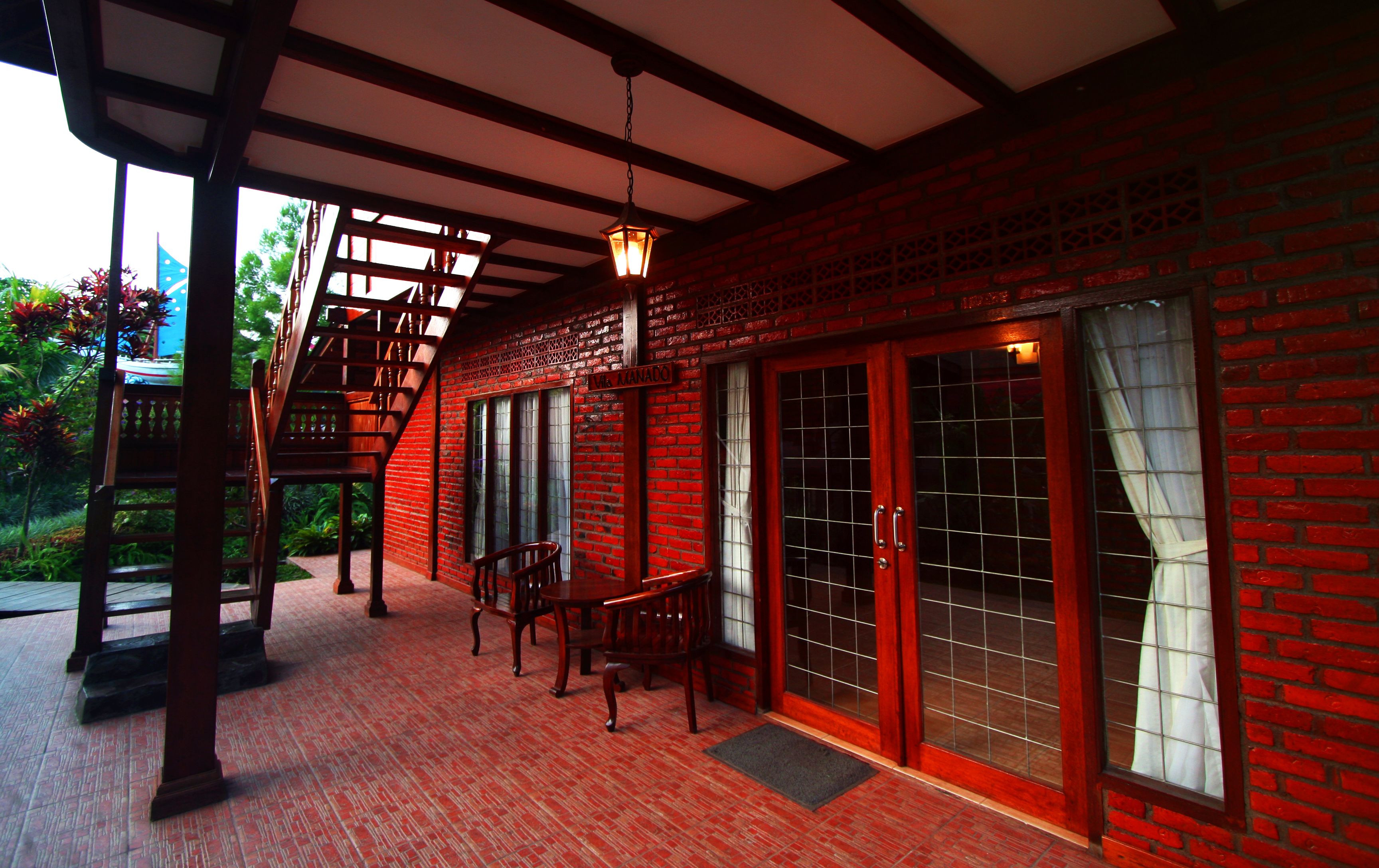 A covered outdoor seating area with a wooden table and chairs, a brick wall, and a lantern.