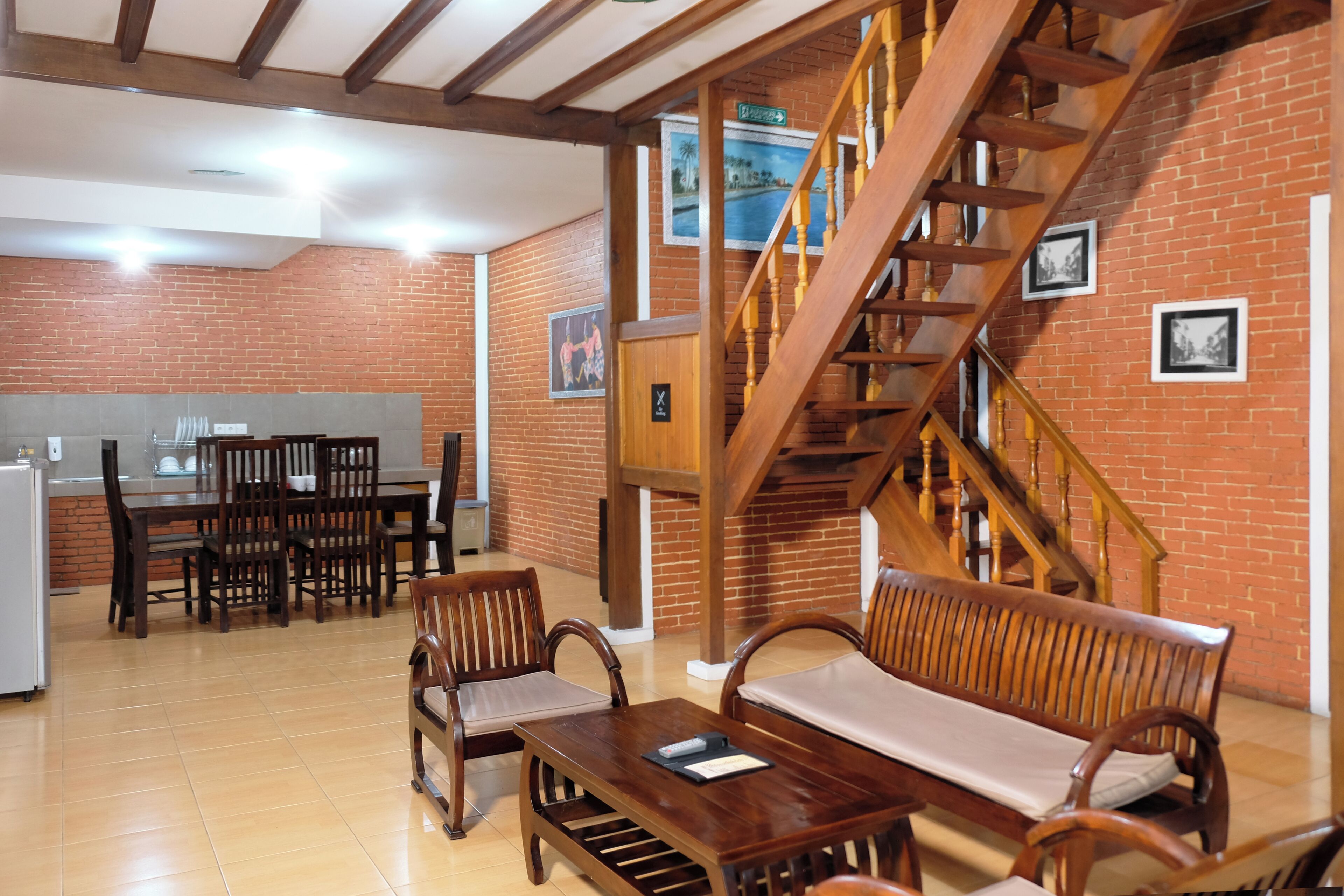 Une pièce spacieuse avec un escalier en bois, un coin repas comprenant des chaises et une table, et un mur en briques orné de tableaux encadrés.
