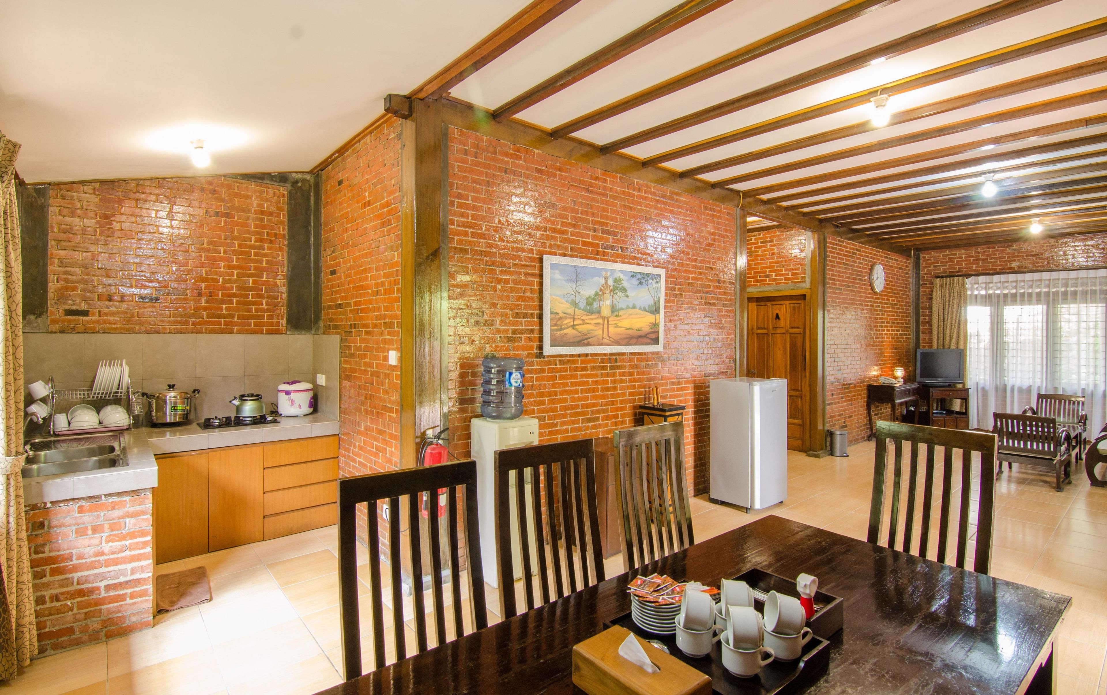A kitchen with a brick wall, wooden beams, a dining area with a table and chairs, and a TV in the background.
