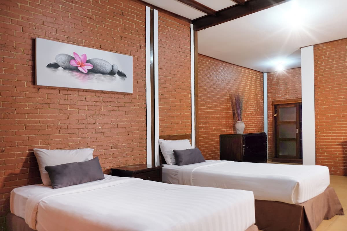 Ein Hotelzimmer mit zwei Betten, einer Ziegelwand, einem Gemälde mit Steinen und einer Blume sowie einem Spiegel, der das Zimmer reflektiert.