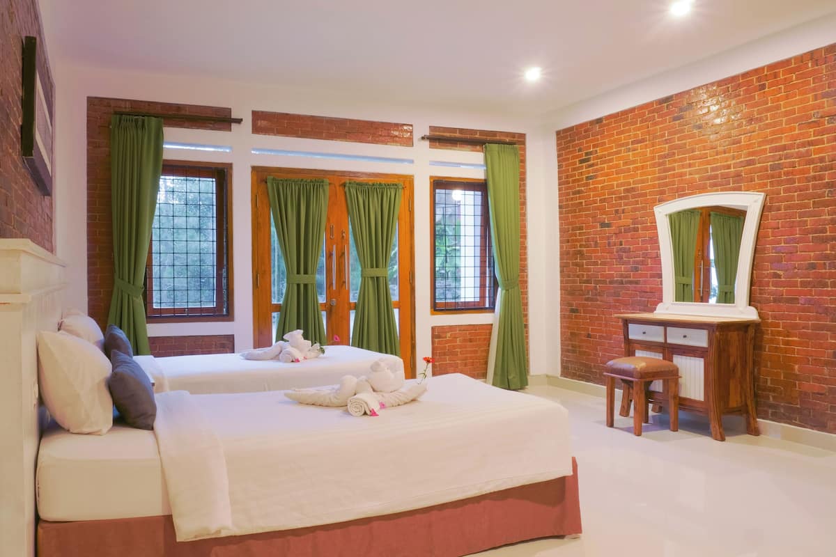 Ein Hotelzimmer mit zwei Betten, grünen Vorhängen, einem Holztisch und einem Spiegel.