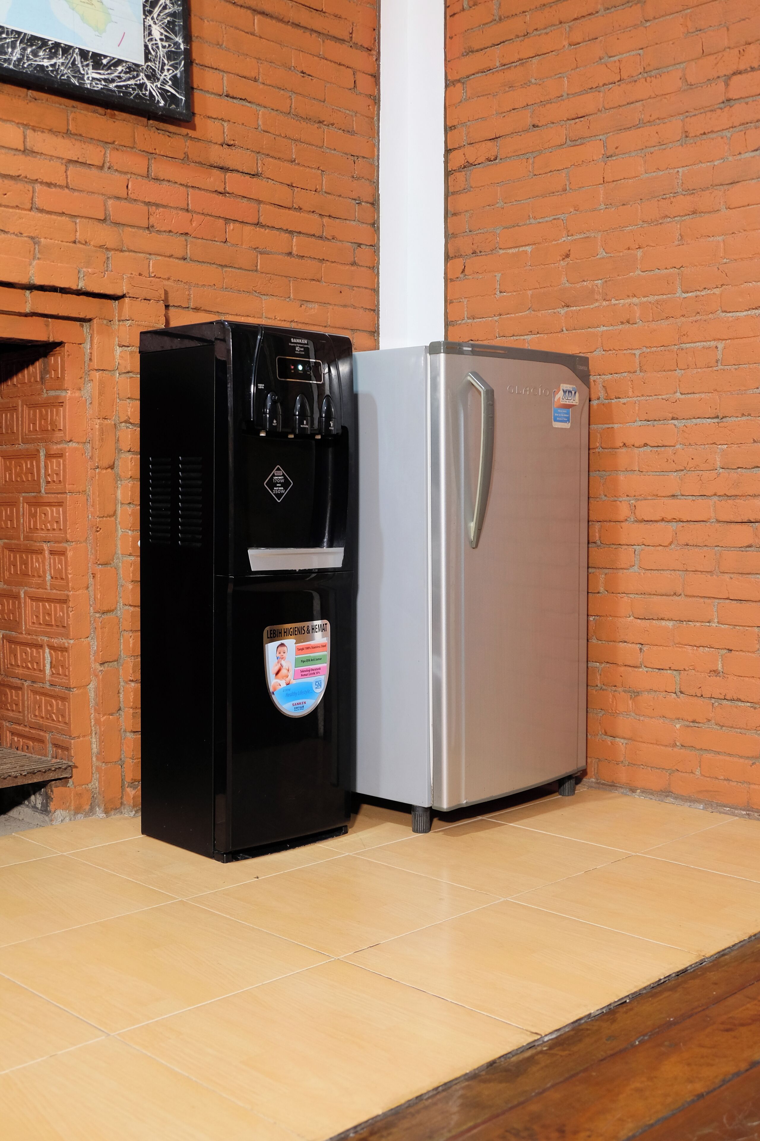 A black refrigerator with a water dispenser and a silver refrigerator next to a brick wall.
