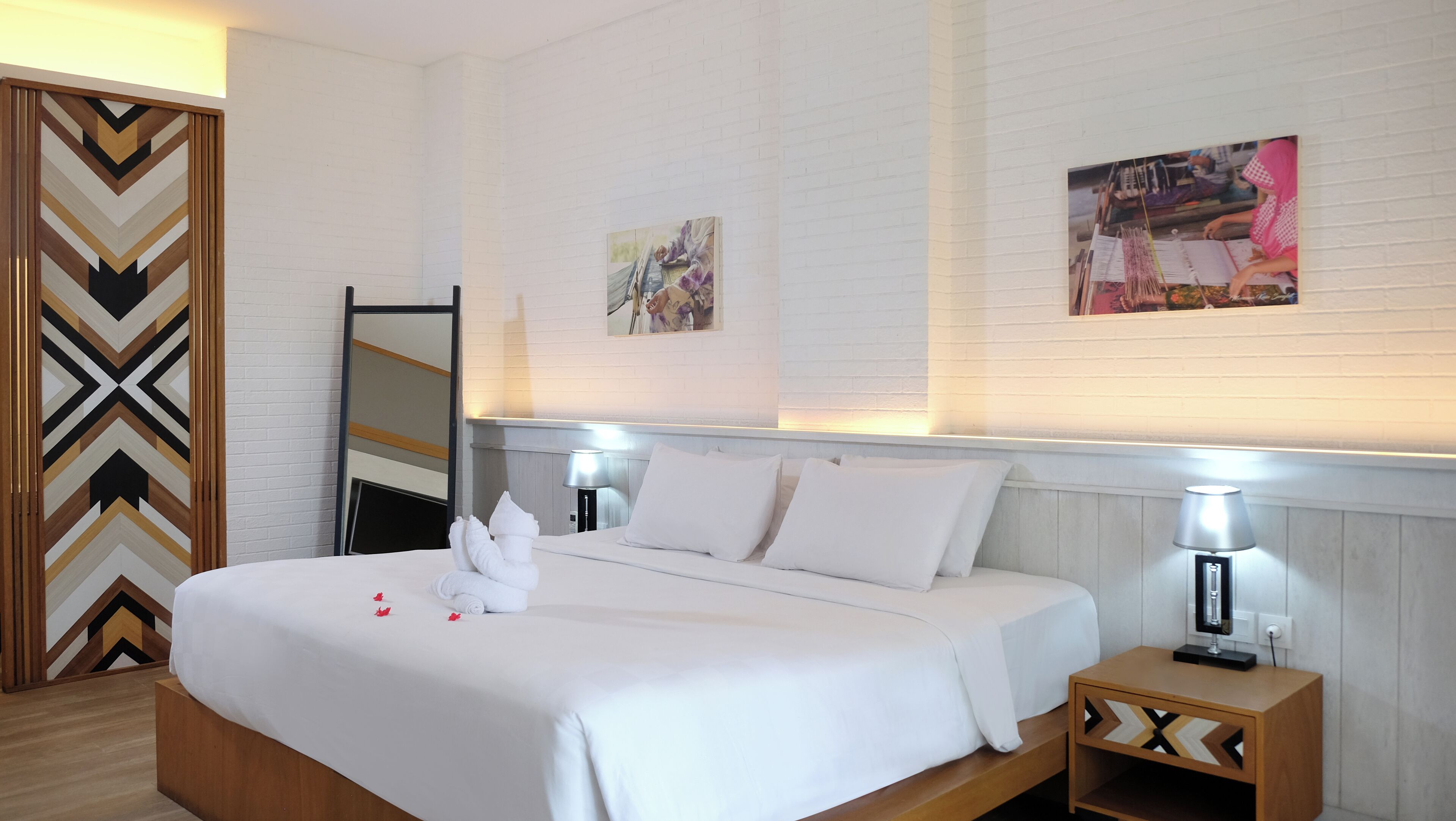 Une chambre d’hôtel avec un lit bien fait, une tête de lit en bois, une table de chevet avec une lampe et deux tableaux encadrés au mur.