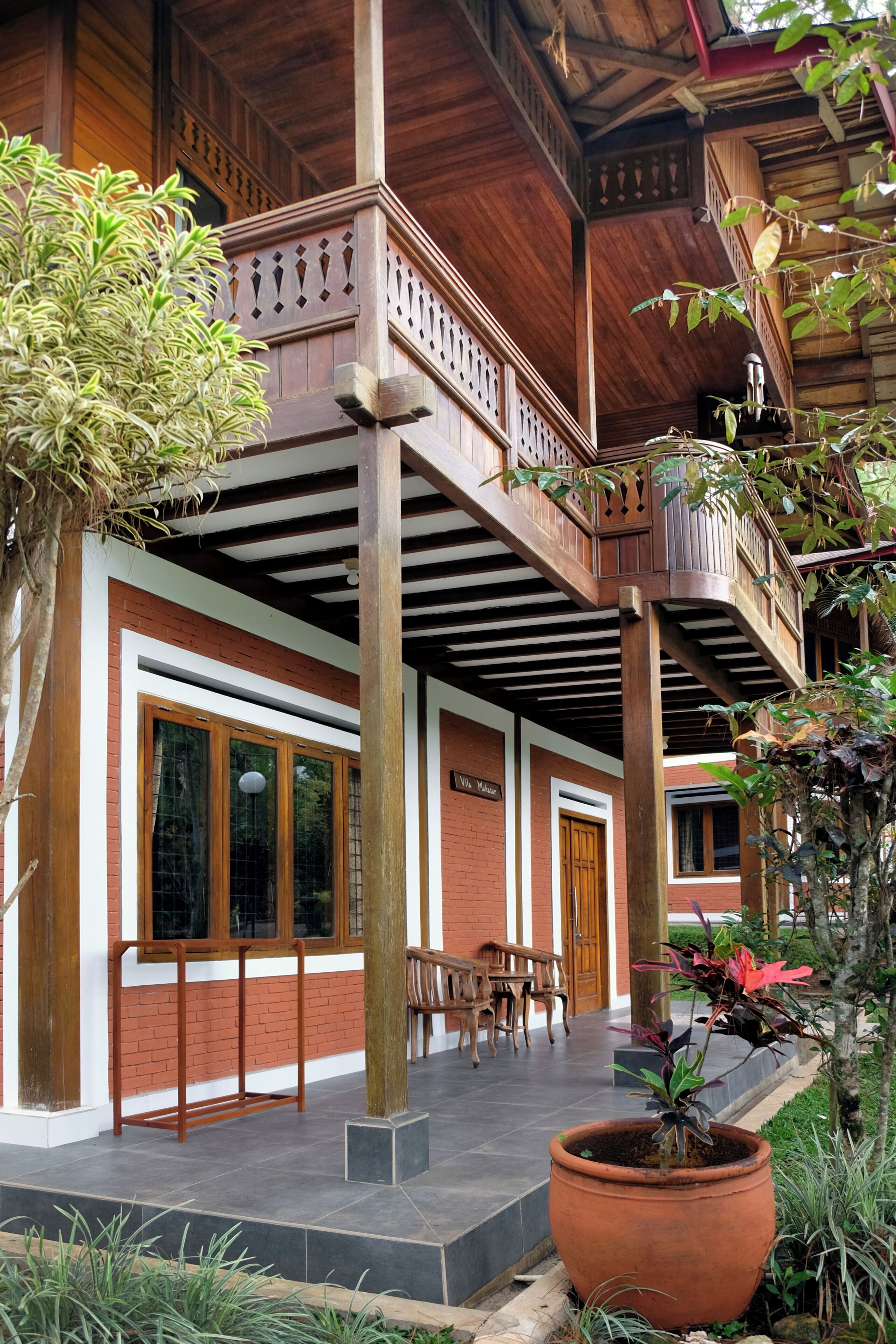 A wooden building with a balcony, a large potted plant, and a brick wall.