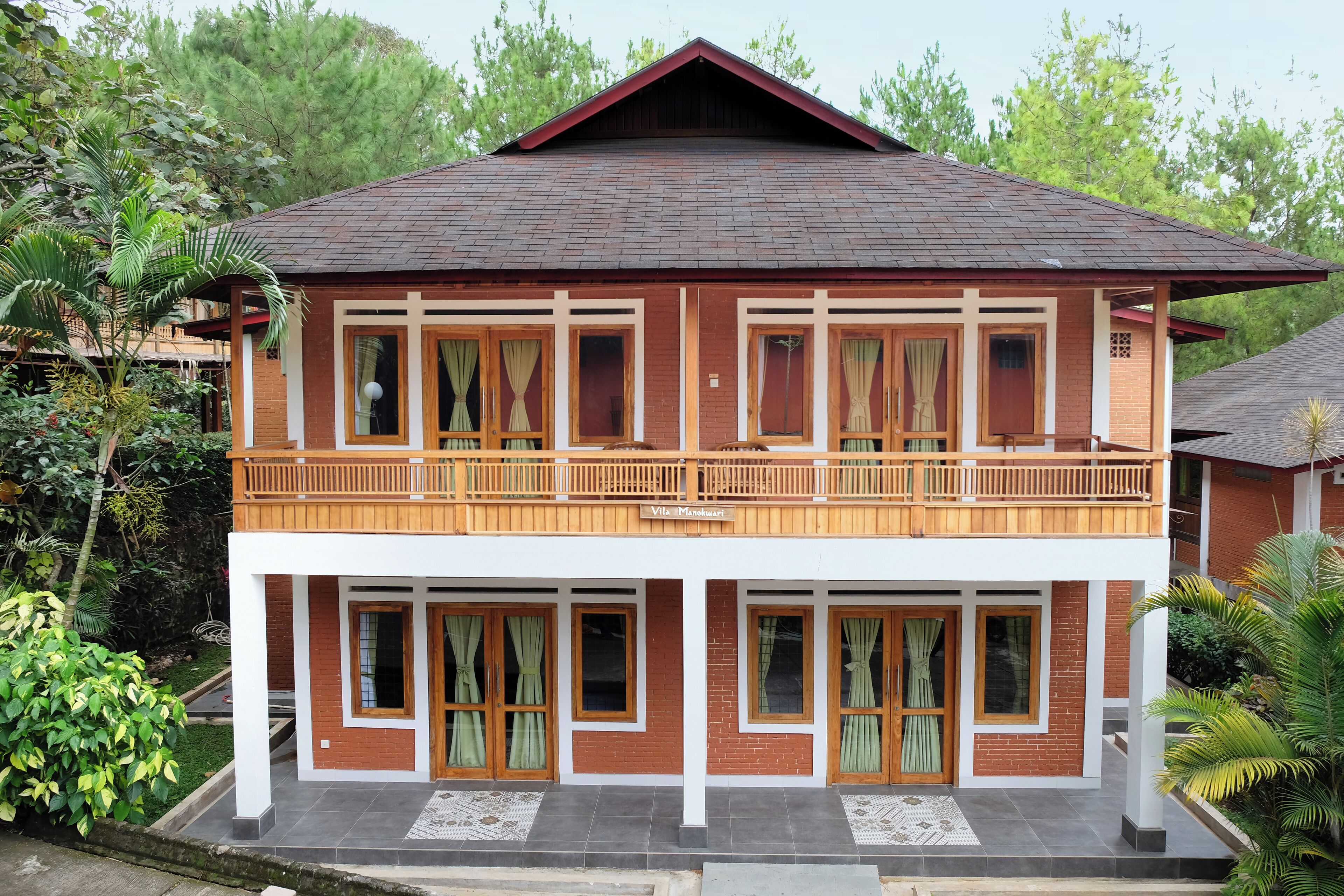 A two-story building with a balcony on the upper floor, surrounded by greenery.