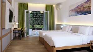 Habitación de hotel con dos camas, un escritorio con silla, una mesita y vistas a zonas verdes a través de una puerta abierta.