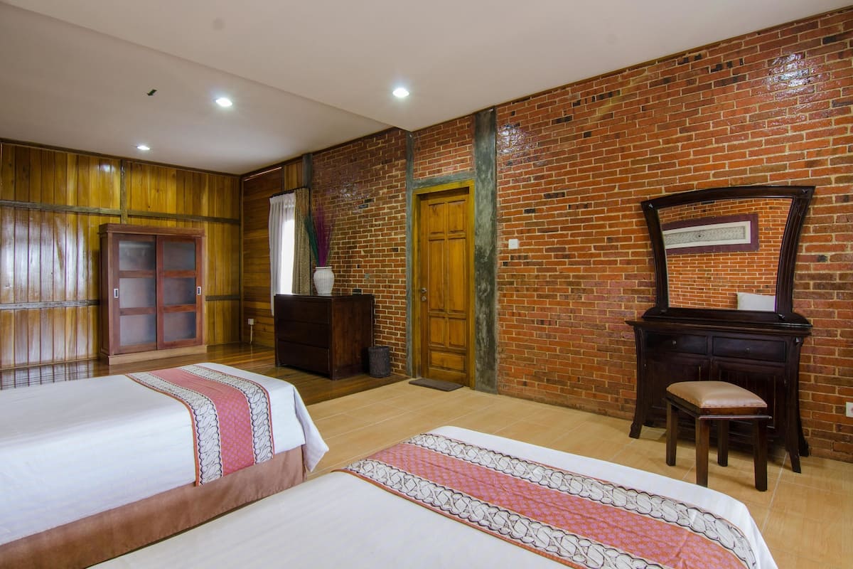 Ein Hotelzimmer mit zwei Betten, Holzwandverkleidung, einer Ziegelwand, einem Holzschrank und einem Spiegel.