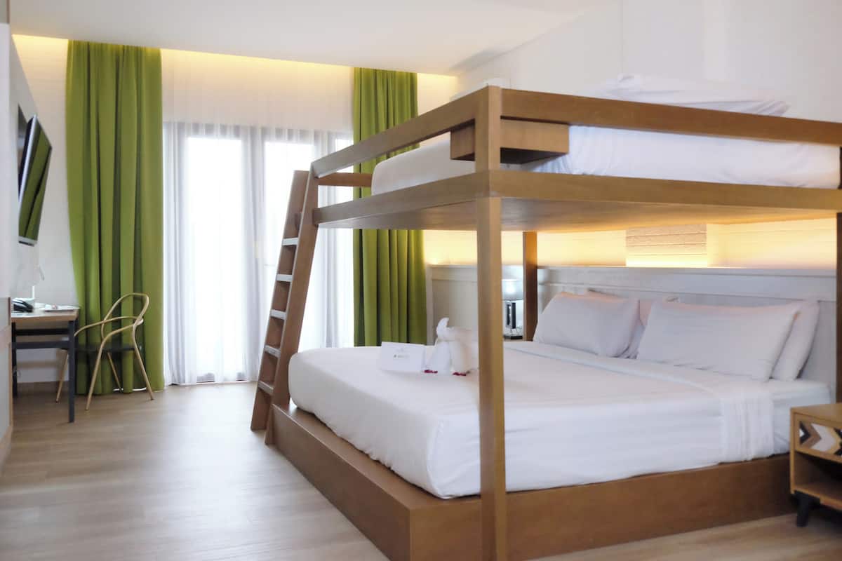 Ein Stockbett mit weißer Bettwäsche, ein Schreibtisch mit Stuhl und ein Nachttisch mit Lampe.