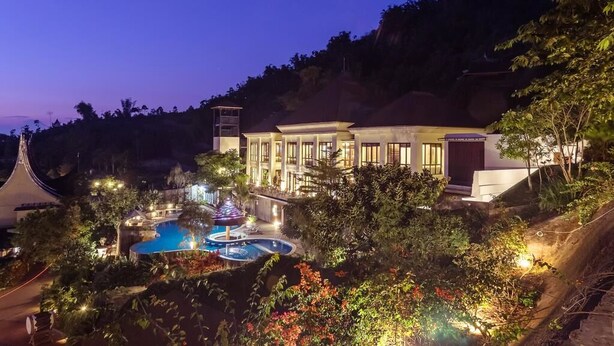 Un resort con un amplio área de piscina, un edificio con múltiples ventanas y abundante vegetación.