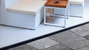 Una habitación moderna con mobiliario de mimbre blanco, un televisor de pantalla plana montado en un panel de madera y dos lámparas colgantes de mimbre.