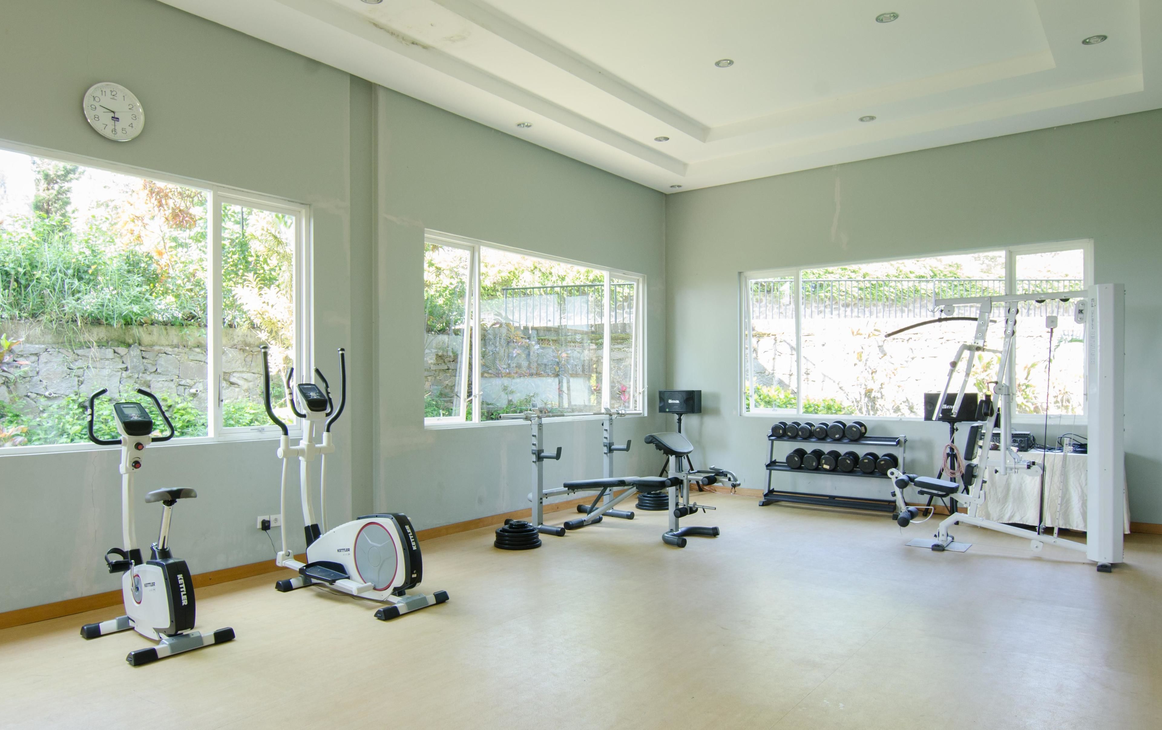 A gym with various exercise equipment, large windows, and a clock on the wall.