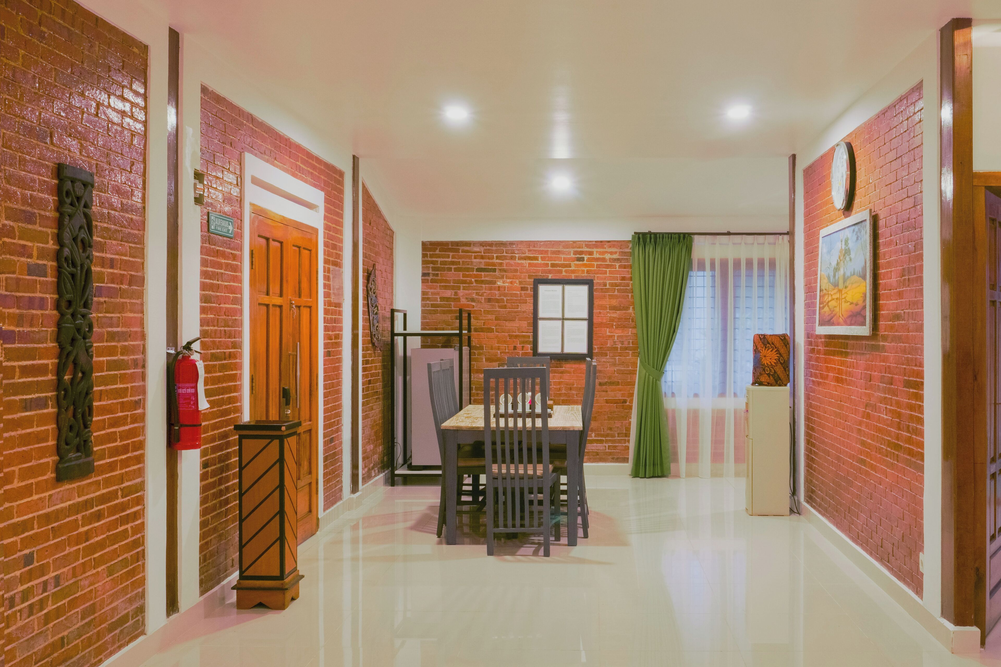 A hallway with a brick wall, a wooden door, a small table with chairs, and a green curtain.