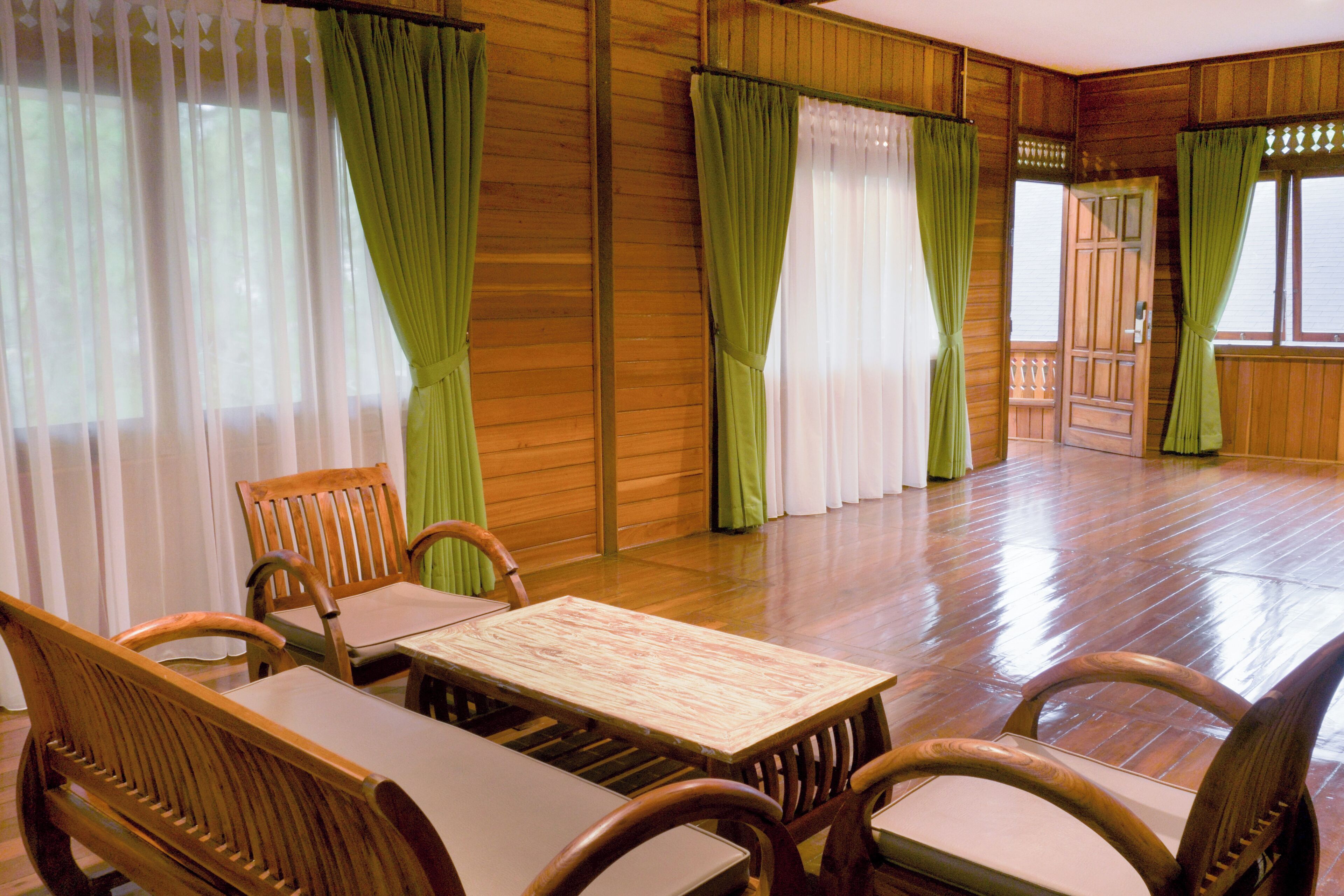 Una habitación con paneles de madera, una mesa de madera con sillas y cortinas verdes.