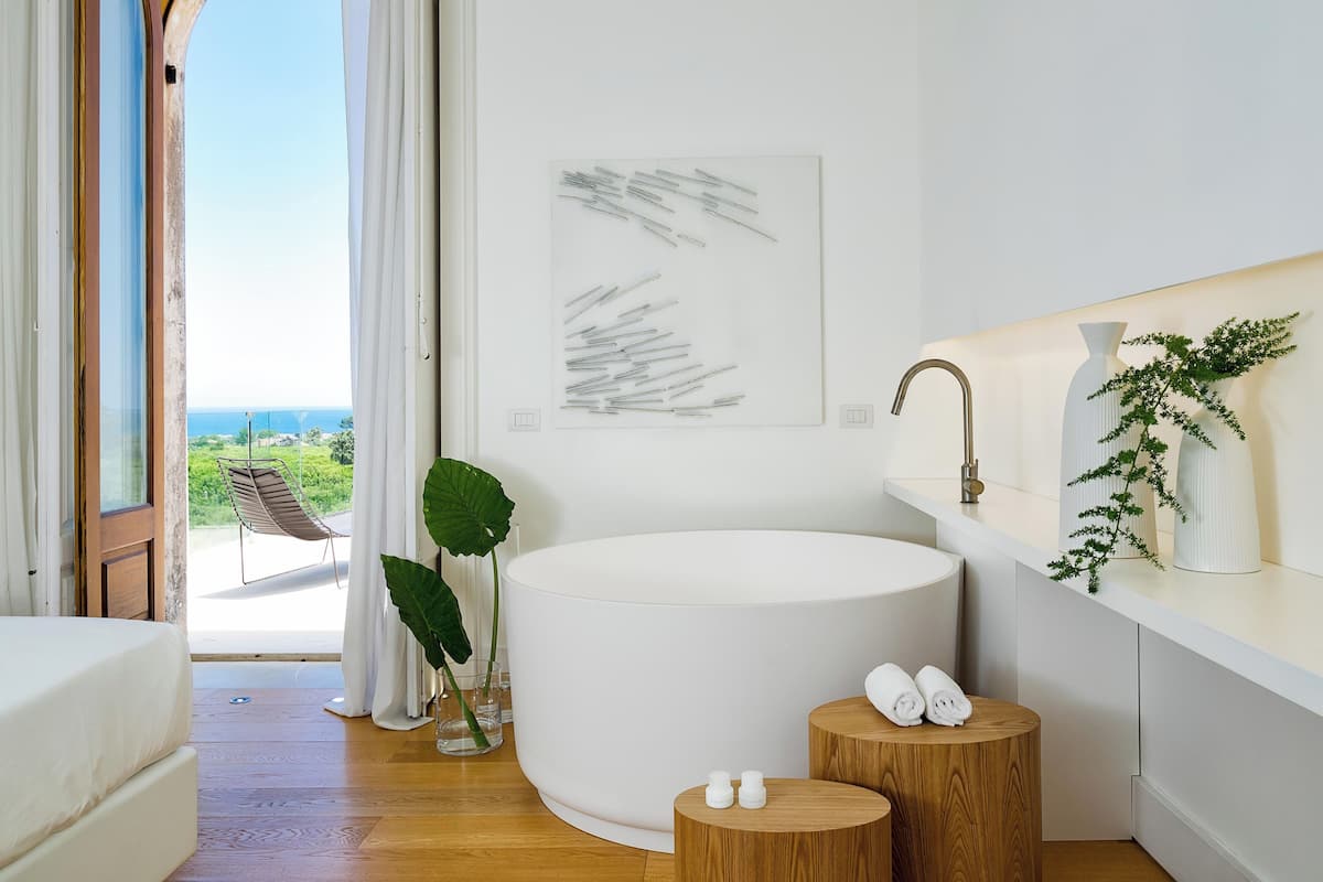 Un baño moderno con una bañera grande, un taburete de madera y vista al mar.