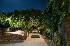 An outdoor patio with a table and chairs, surrounded by greenery and stone walls.