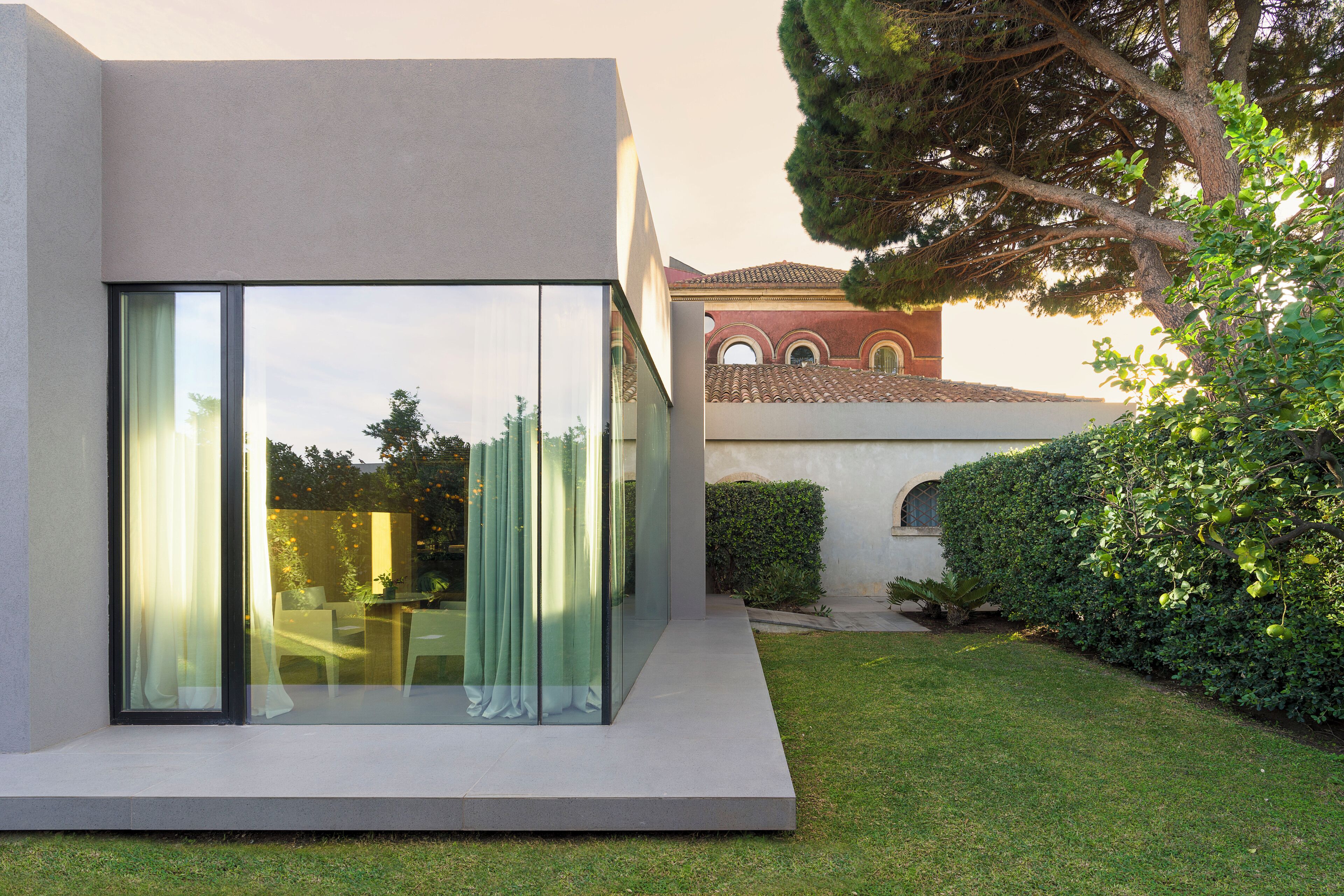 A modern house with a glass facade, a well-maintained lawn, and a large tree.