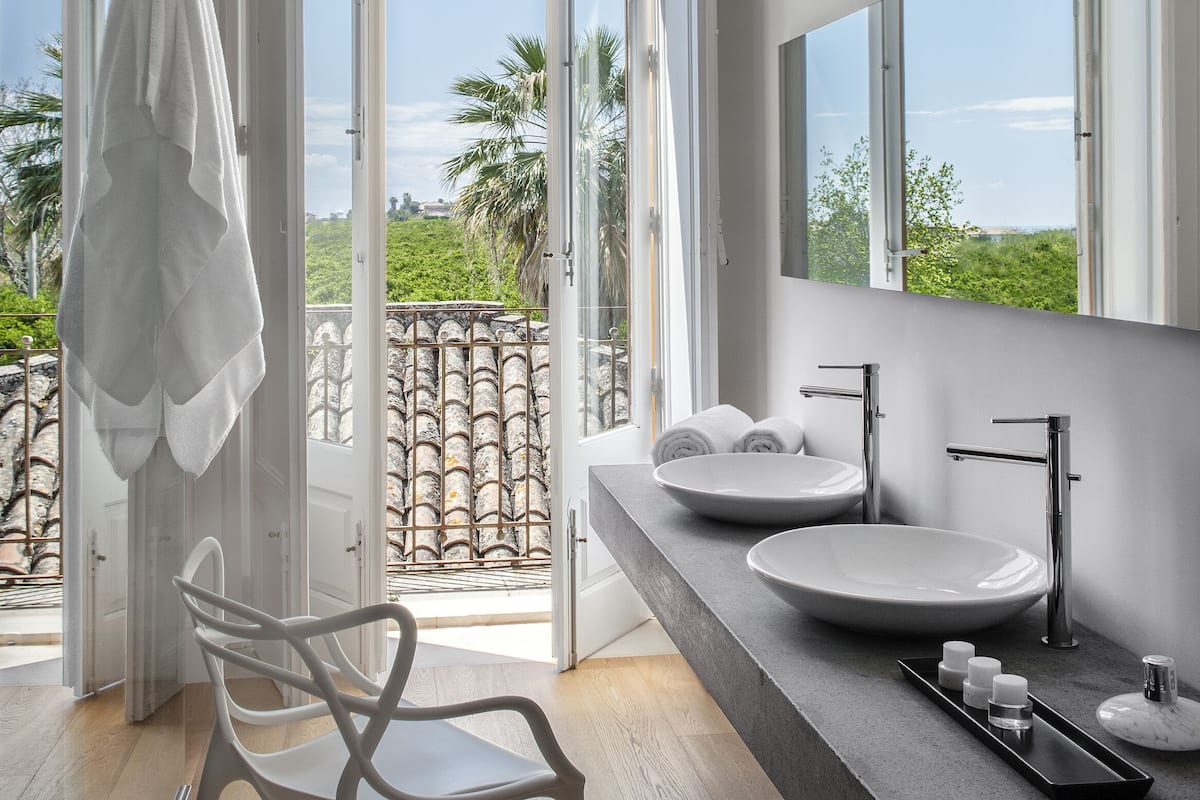 Un baño moderno con un ventanal grande, un lavabo blanco y una silla.