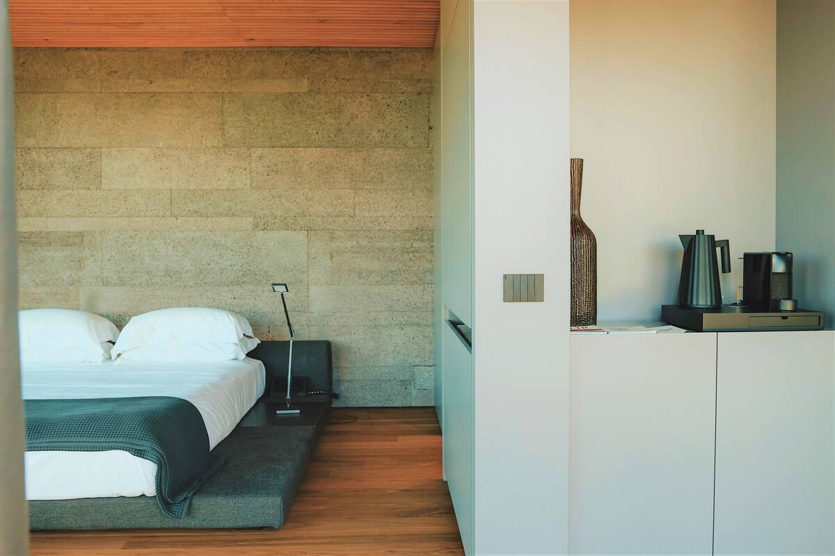Un dormitorio moderno con cama, mesita de noche, lámpara y un armario blanco.
