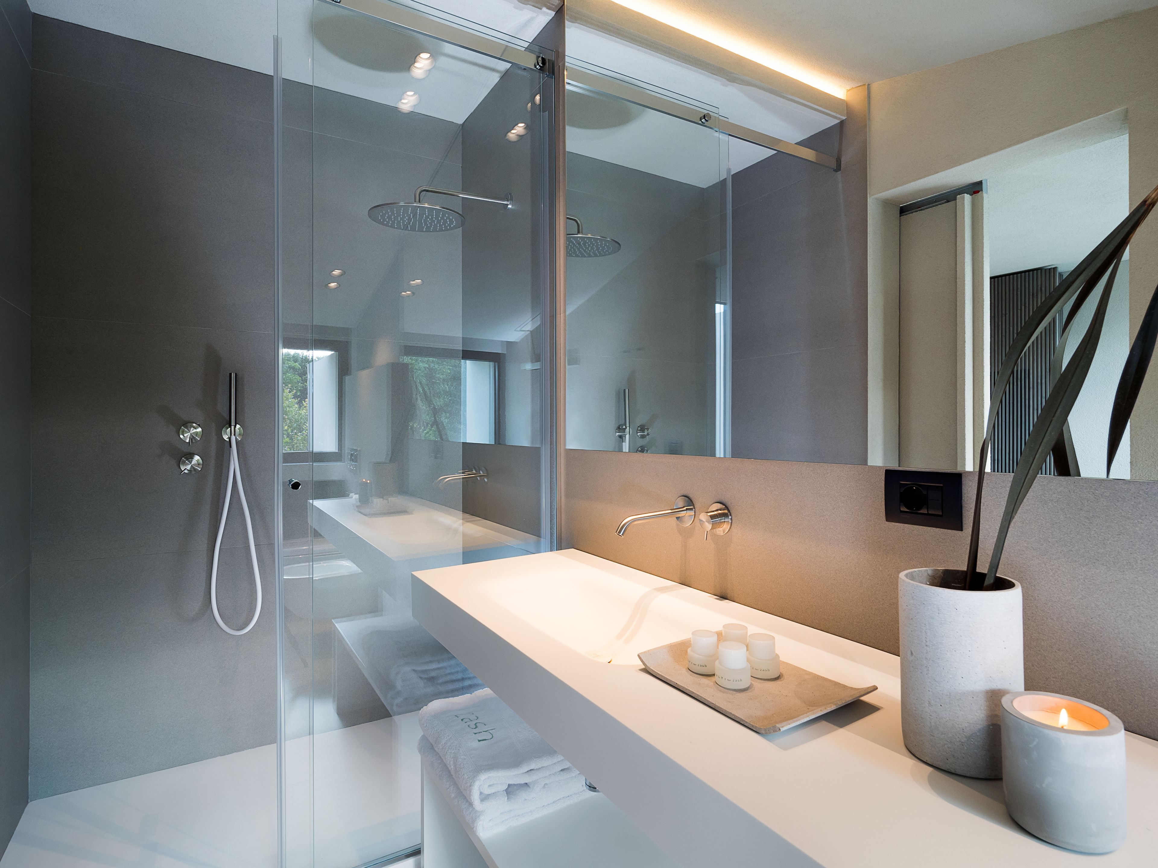 Un baño moderno con ducha de vidrio, tocador blanco con espejo y una vela en la encimera.
