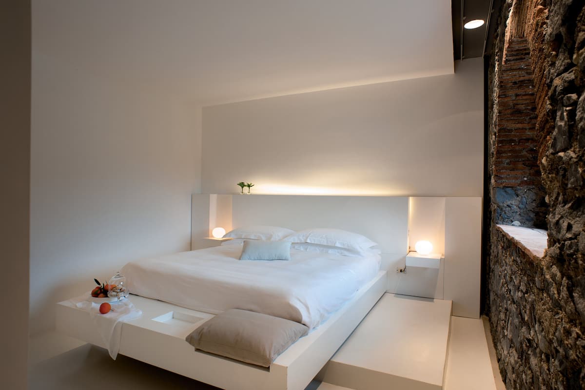 Un dormitorio moderno con una cama blanca, mesitas de noche y una pared decorada con ladrillos.