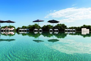 A clear pool with lounge chairs and umbrellas, surrounded by greenery.