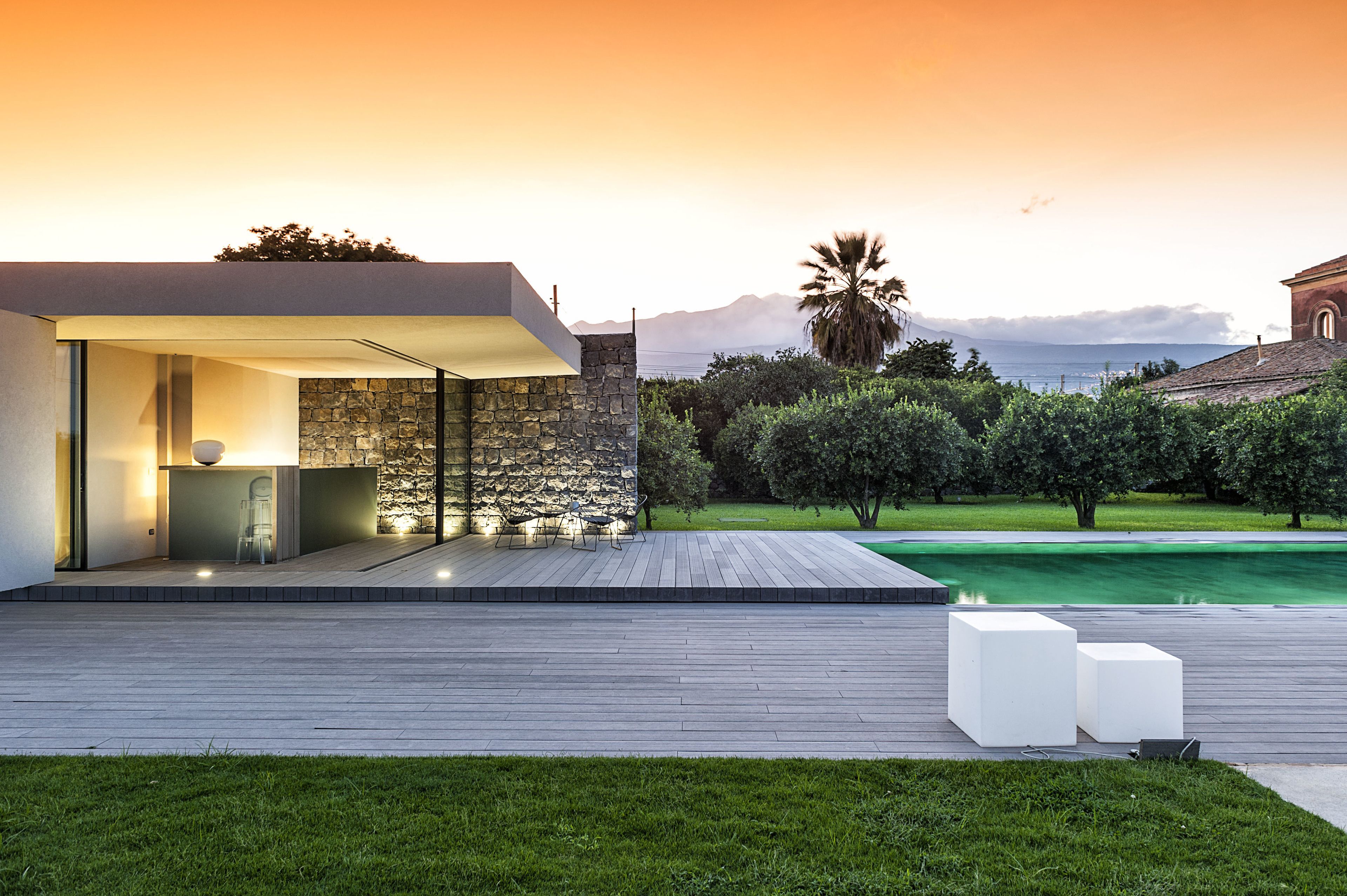 Ein modernes Haus mit einer Stein-Fassade, einer Holzterrasse und einem Pool.