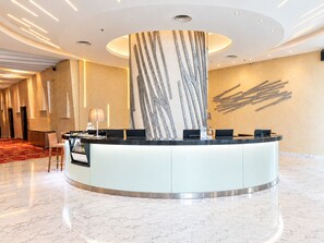 A modern reception desk with a curved design, a marble floor, and a wall with abstract art. - Holiday Inn Express Jakarta Pluit Citygate by IHG (Jakarta)