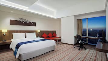 A hotel room with a bed, desk, chair, and a large window.