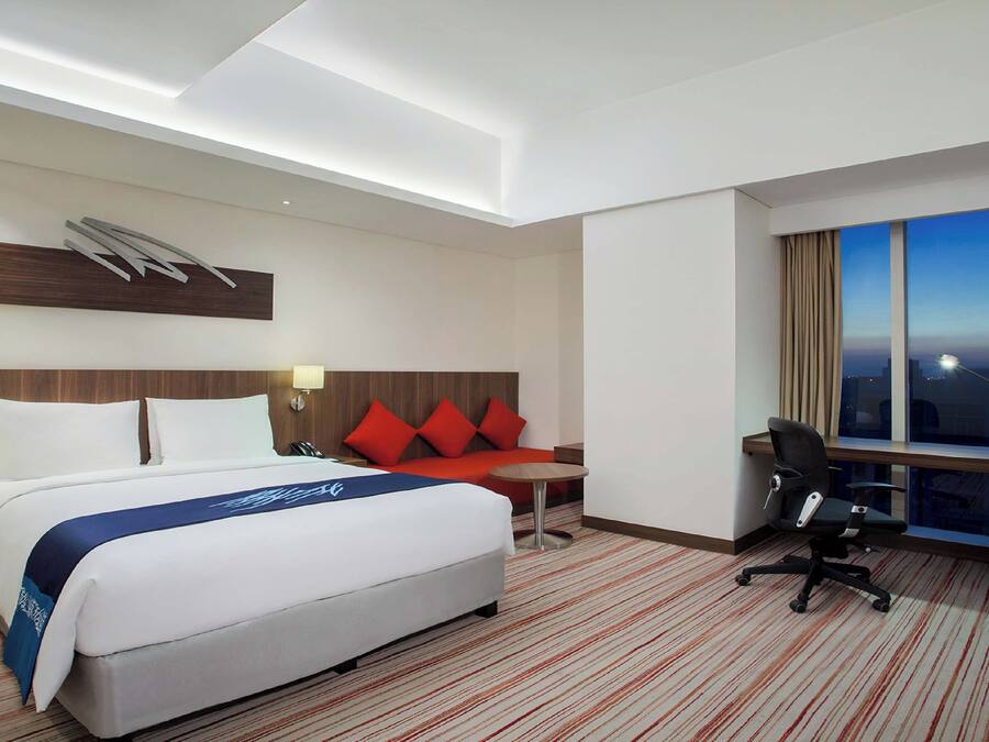 A hotel room with a bed, desk, chair, and a large window.